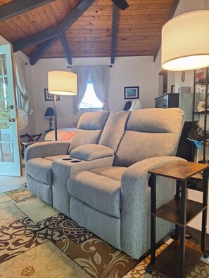 Un canapé gris dans une pièce dont le plafond est en bois, avec un lampadaire et un tapis à motifs.