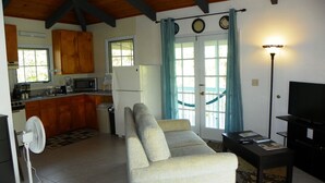 Un espacio habitable compacto con kitchenette, sofá, televisor y ventilador.