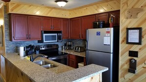 A kitchen with wooden cabinets, granite countertops, a stainless steel refrigerator, a microwave, a stove, and a sink.
