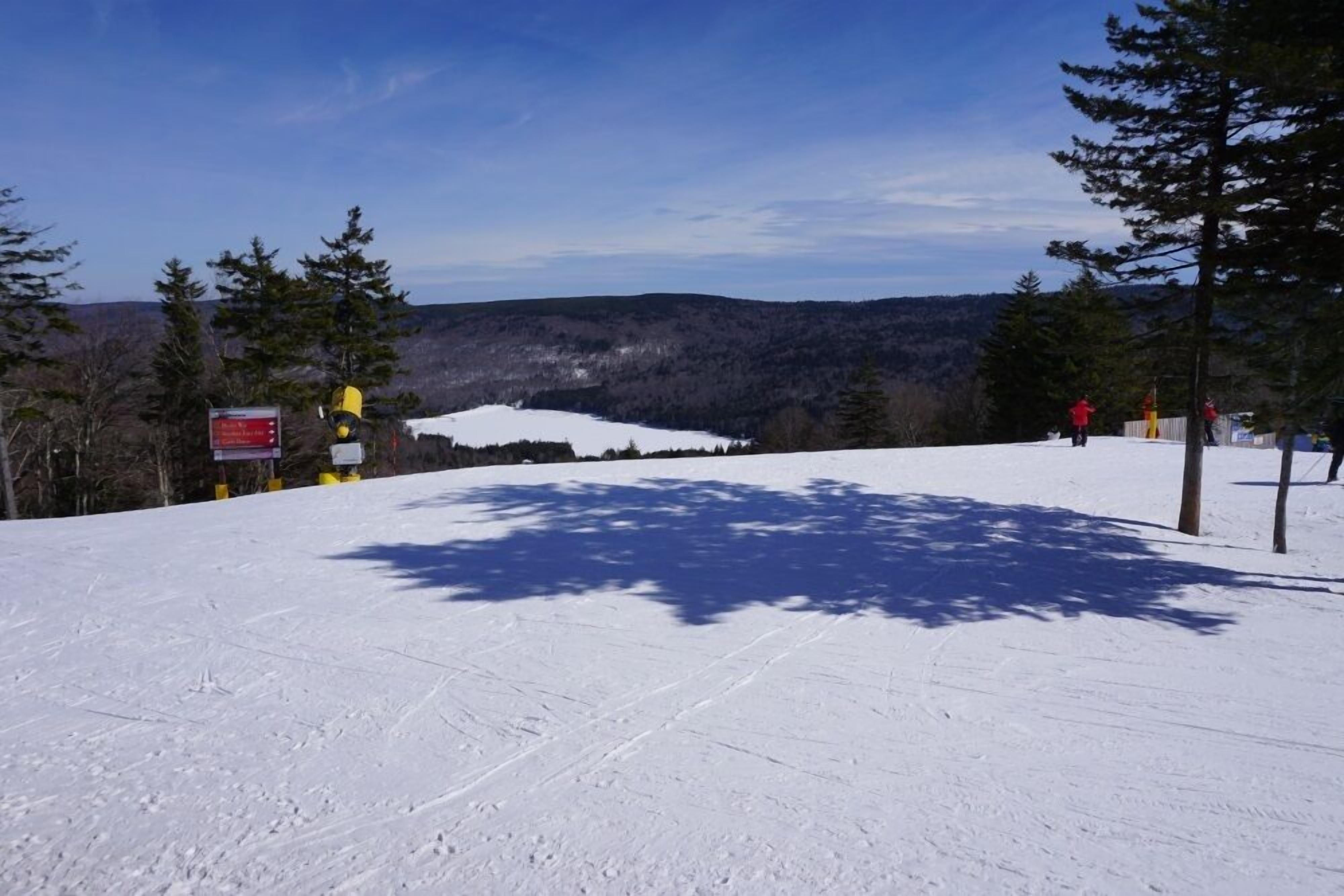 A snow-covered ski slope with a clear sky and distant mountains.
