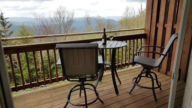 A wooden deck with a table and two chairs, overlooking a mountainous landscape.