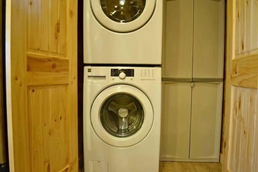 A stacked washer and dryer unit in a wooden-finished room.
