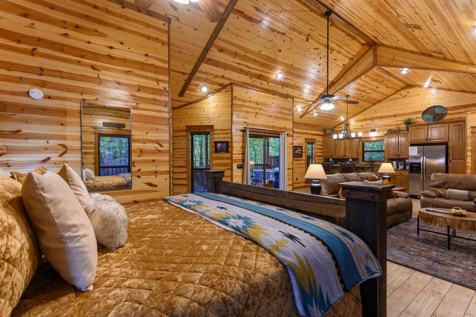 A log cabin interior with a large bed, a sofa, a dining area, and a kitchen.