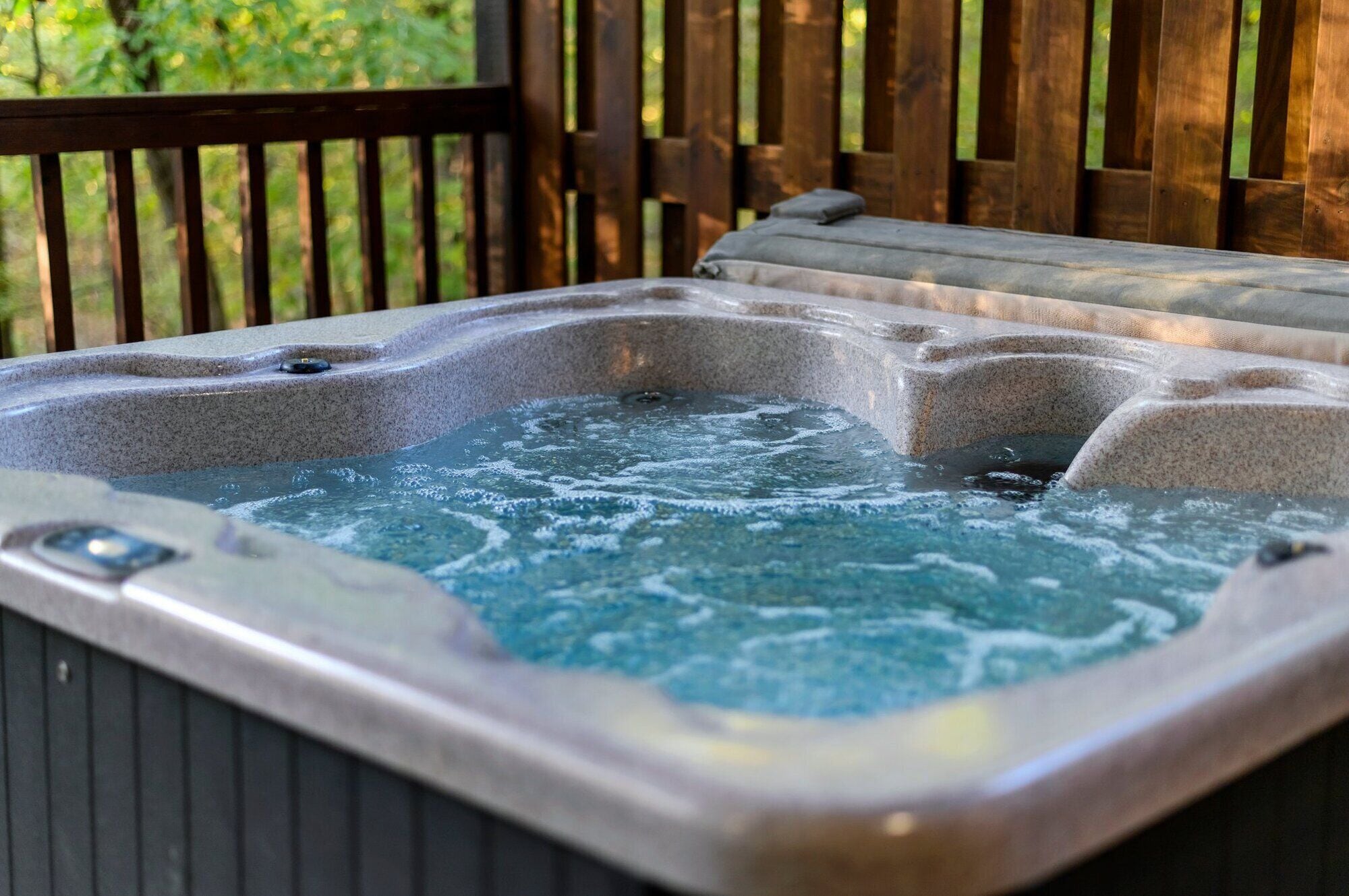 Un jacuzzi con una terraza de madera y una valla de madera al fondo.