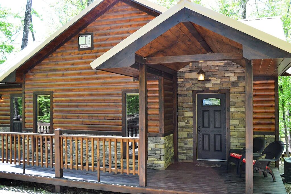 Una cabaña de troncos con porche, chimenea de piedra y mobiliario de exterior.