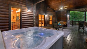 Eine Holzhütte mit Whirlpool, einer Terrasse mit Tisch und Stühlen sowie einem Deckenventilator.