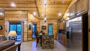 Ein Blockhaushaus-Interieur mit einer Steineninsel, Holzschränken und einem Edelstahlkühlschrank.