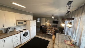 Une cuisine avec des meubles blancs, une cuisinière et un four à micro-ondes. On y trouve une table à manger avec des chaises et un tapis noir.