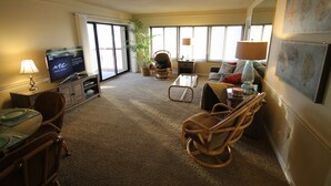 Ein Wohnzimmer mit Fernseher, Esstisch, Stühlen, einer Couch, einem Couchtisch und einer Zimmerpflanze.