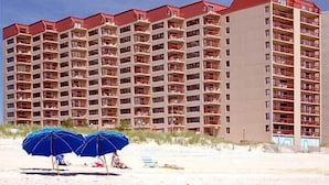 Ein mehrstöckiges Hotel mit Balkonen in Strandnähe, mit Sonnenschirmen.