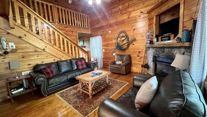 A wooden cabin interior with a staircase, a fireplace, a sofa, and a television.