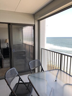 Enjoy the serene view of the ocean from this balcony with a glass table and two chairs.