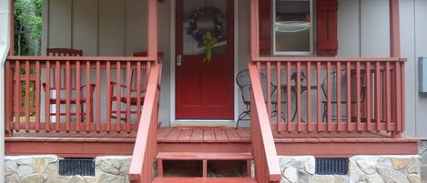 Une maison avec une porte d’entrée rouge, une véranda avec des balustrades rouges et un mur en pierre.