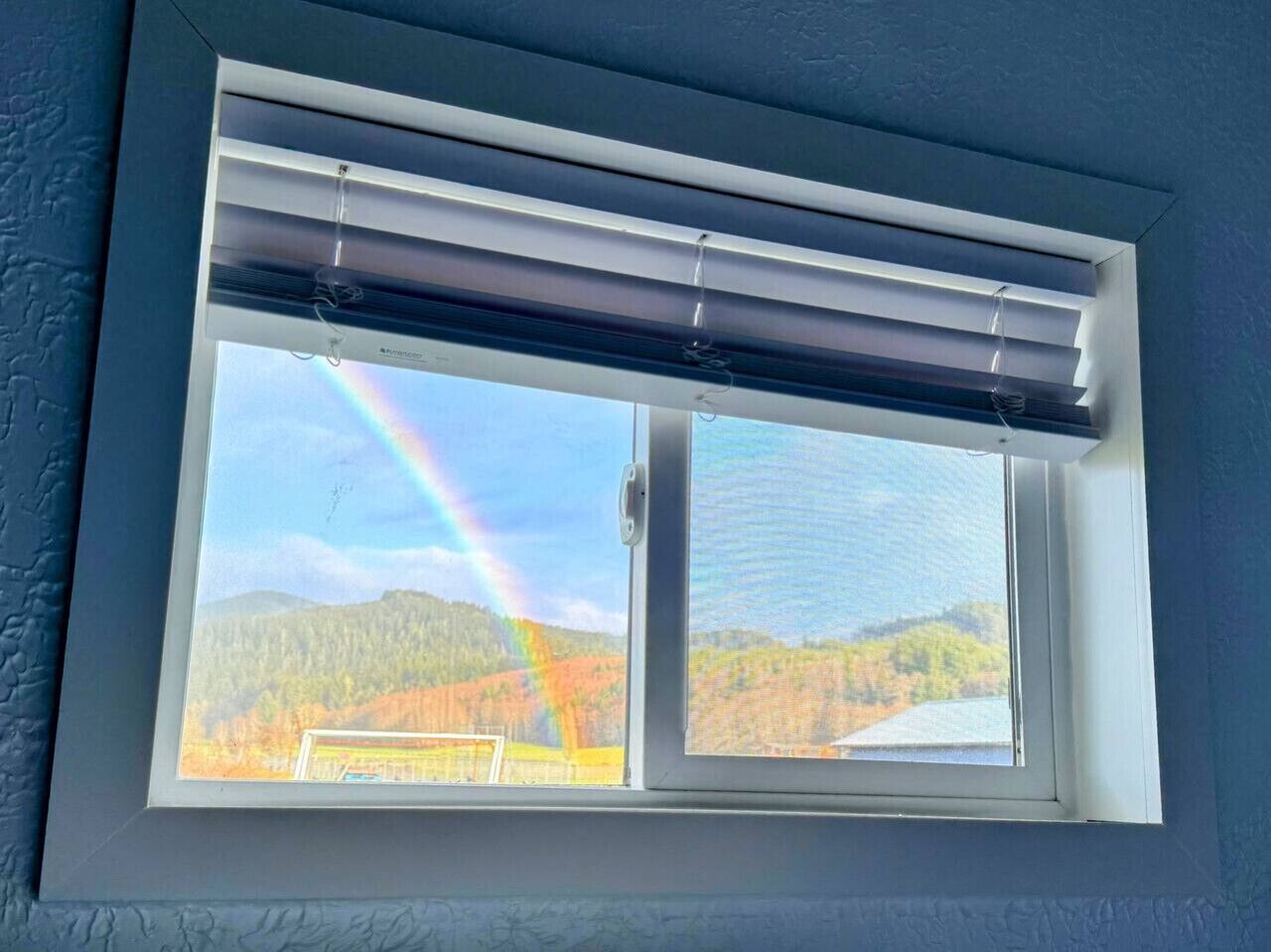Una ventana con vista a un arcoíris sobre un paisaje boscoso.