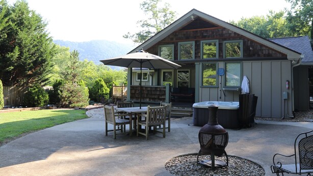 Una cabaña de madera con un área de patio que incluye una mesa, sillas, un jacuzzi y un paraguas grande.