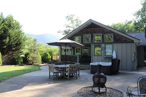 Une cabane en bois dotée d’un patio comprenant une table et des chaises, un jacuzzi et un grand parasol.