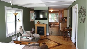 Un salón espacioso con chimenea, un televisor montado encima y una zona de comedor al fondo.