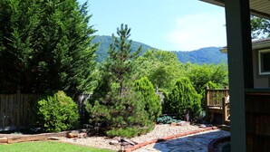 Un sendero de piedra que lleva a una terraza de madera, rodeada de exuberante vegetación y con una montaña al fondo.