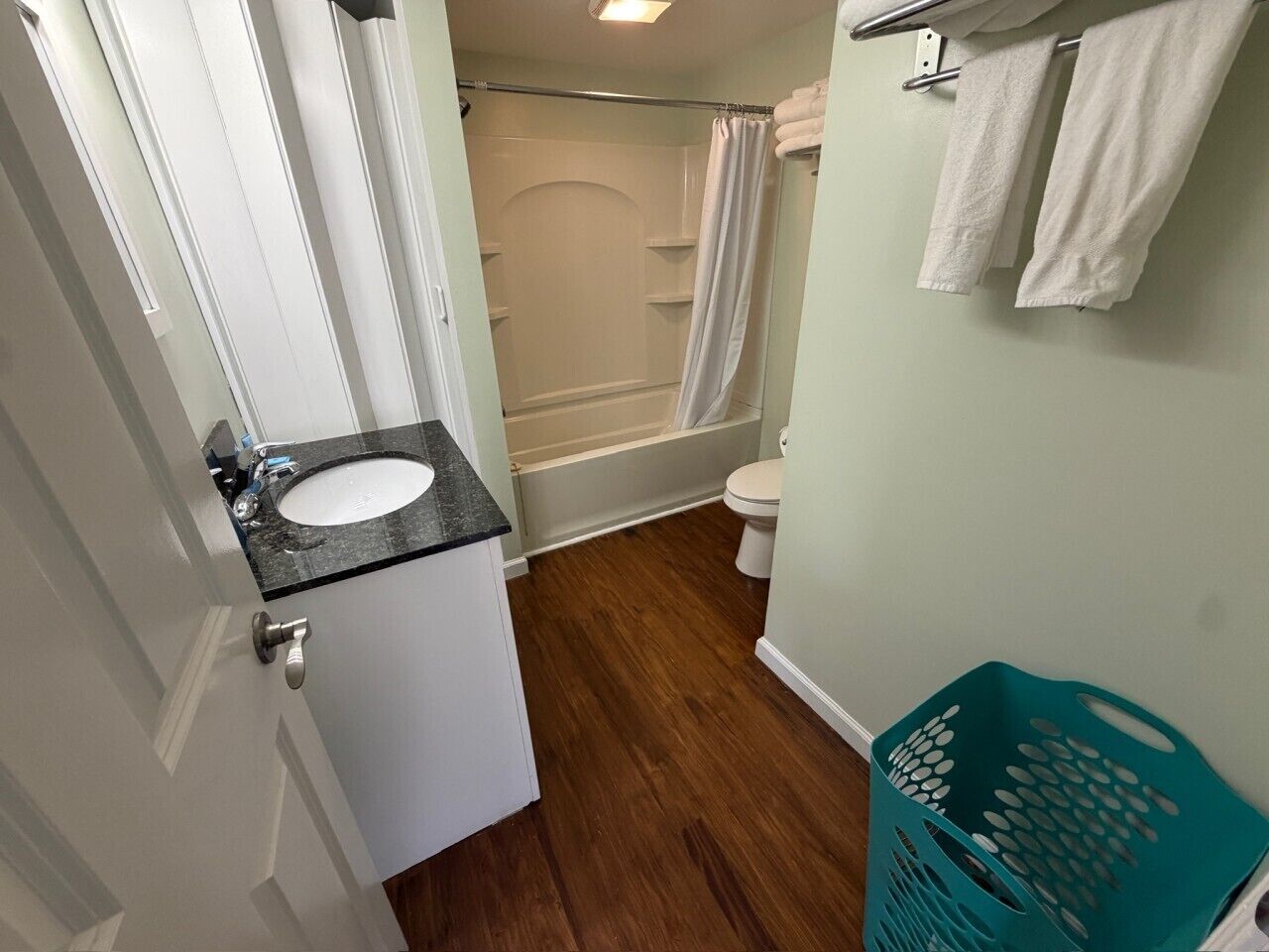 Une salle de bain équipée d’un lavabo, de toilettes, d’une douche et d’un panier à linge de couleur turquoise.