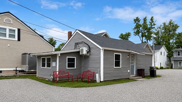 A single-story house with a gray exterior, a chimney, and a gravel driveway.