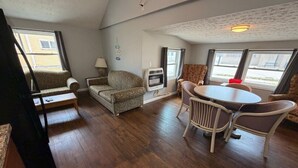 A room with a wooden floor, a round table with chairs, a sofa, and a window with curtains.