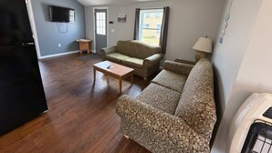 A living room with a sofa set, a coffee table, a television, and a window with curtains.