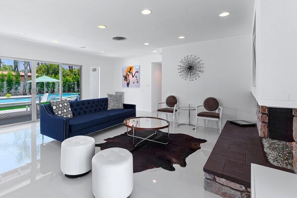 A modern living room with a blue sofa, white ottomans, a glass coffee table, and a stone fireplace. - Orangetini Mid-Century Hollywood Regency Style Retreat - Last Minute Specials! (Palm Springs)