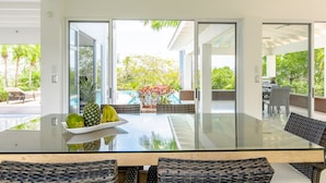 A modern kitchen with a glass dining table, a fruit bowl, and a view of a pool and garden. - Luxurious villa with panoramic views and breathtaking private infinity pool !!! (Tamarindo)