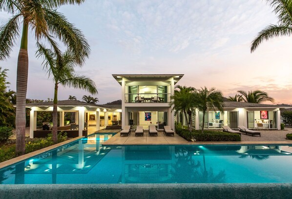 Une maison moderne à deux étages, dotée d’une piscine, d’un espace salon extérieur et d’un patio couvert.