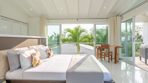 A modern bedroom with a large bed, a wooden desk, and a view of palm trees through large glass doors. - Luxurious villa with panoramic views and breathtaking private infinity pool !!! (Tamarindo)