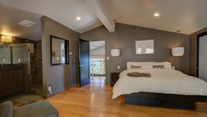 Une chambre à coucher moderne avec un grand lit, un coin salon avec un banc et une vue sur l’extérieur.