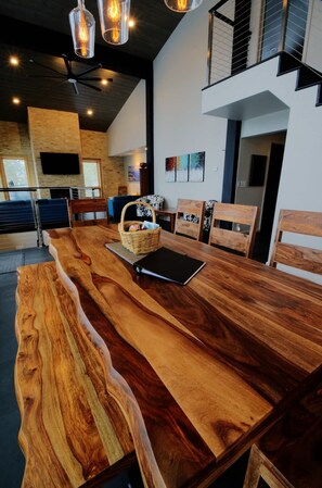 Une cuisine moderne avec un grand îlot central en bois, une table à manger et des chaises. Un téléviseur est fixé au mur et un panier se trouve sur l’îlot.
