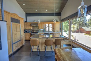 A modern kitchen with wooden cabinets, a central island with bar stools, and large windows offering a view of the outdoors.