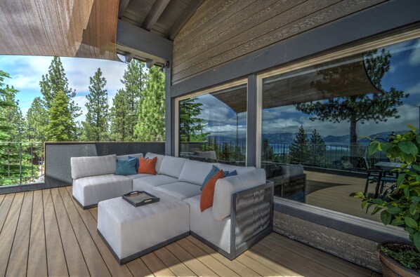 A modern outdoor living space with a sectional sofa, a dining table, and a large window offering a view of a forest and mountains.