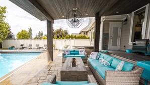 En overdækket udendørs terrasse med pool, fletmøbler og en lysekrone.