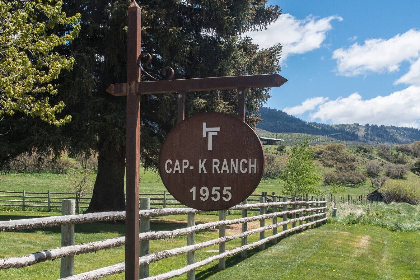 Señal de Cap-K Ranch con una valla de madera rústica y un paisaje montañoso.