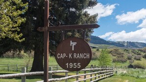 Placa de Cap-K Ranch, com cerca de madeira rústica e paisagem de montanhas ao fundo.