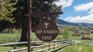 Señal de Cap-K Ranch con una valla de madera rústica y un paisaje montañoso.