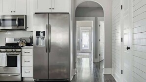 A modern kitchen with stainless steel appliances, white cabinetry, and a wooden floor. - 1-Story Family Home,  Fenced Yard, Grill, Parking | Sleeps 10, 5 Mins to Five Points & Nissan Stadium, Smart TVs, Pet-Friendly Yard, Patio for BBQs, Ideal Nashville Getaway for Families, 24 Hr Hospitality (Nashville)