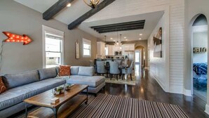 A modern living room with a sofa, coffee table, and striped rug. There is a kitchen in the background with a dining area. - 1-Story Family Home,  Fenced Yard, Grill, Parking | Sleeps 10, 5 Mins to Five Points & Nissan Stadium, Smart TVs, Pet-Friendly Yard, Patio for BBQs, Ideal Nashville Getaway for Families, 24 Hr Hospitality (Nashville)