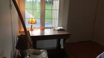 A room with a wooden table, a lamp, a pitcher, and a window with blinds.