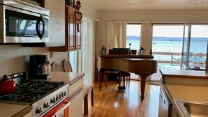 A kitchen with a stove, oven, and microwave, a dining area with a piano, and a view of the sea through large windows. - Lakeside fling! Same day bookings accepted with a VRBO reservation. Terms apply (Canandaigua)