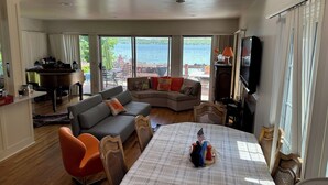 A spacious living room with a grand piano, a sofa, and a dining table set for four. - Lakeside fling! Same day bookings accepted with a VRBO reservation. Terms apply (Canandaigua)