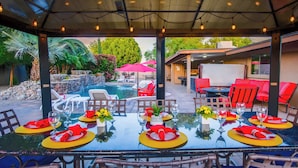 An outdoor dining area with a glass table, red and yellow placemats, and white chairs.