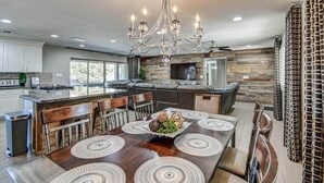 A modern kitchen with a central island, a chandelier, and a dining area with a large table and chairs.