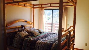 A wooden four-poster bed with a patterned bedspread and pillows, a window with curtains, and a view of a wooden deck outside. - Get Out Of The Heat And Enjoy The Mountain Air,  Catch Trophy Trout, Relax (panguitch)