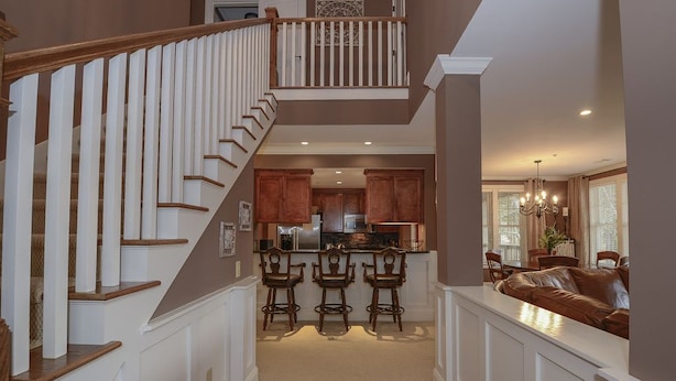A spacious living area with a staircase leading to a second floor, a kitchen with bar stools, and a seating area with a brown leather couch. - WOW! 30% Off Until Oct. 1st | Walk to Ritz, Golf Front, 3 King Beds, Book Now (Greensboro)