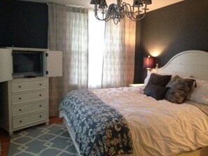Relax in a comfortable room with a neatly arranged bed, television, and chandelier.