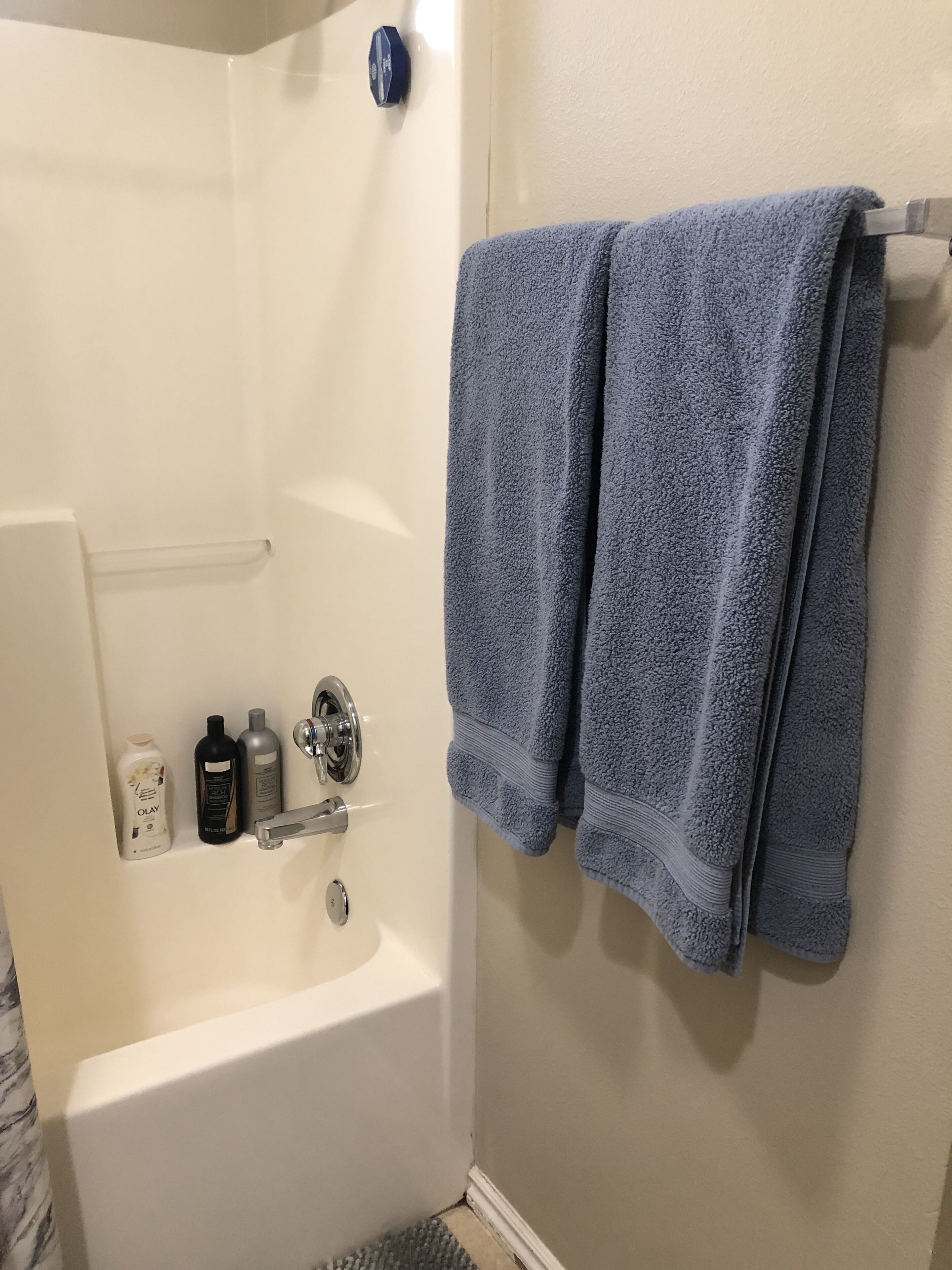 A bathroom with a bathtub, two towels, and three toiletries on the wall.