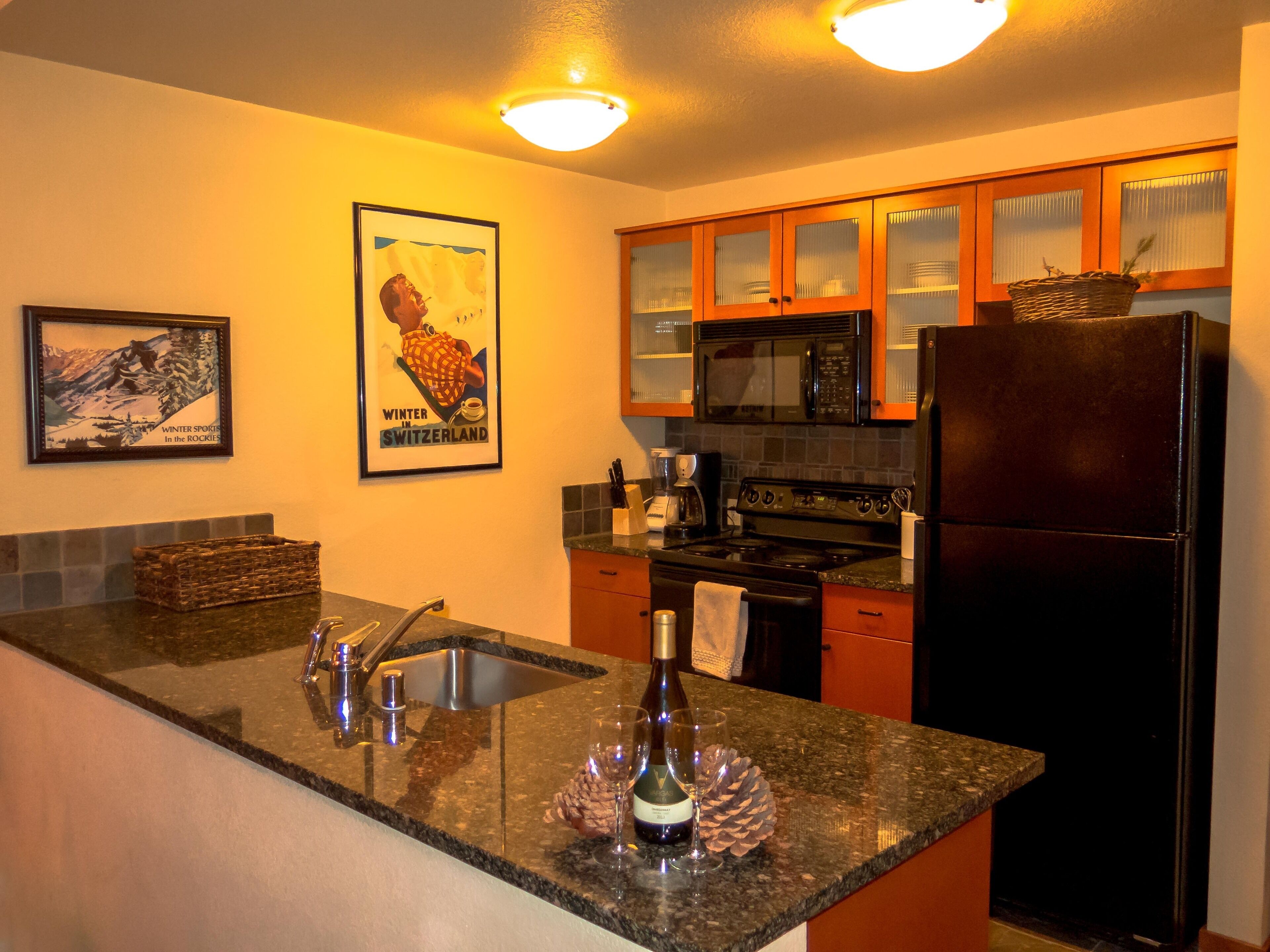A kitchen with granite countertops, stainless steel appliances, wooden cabinets, and a framed poster on the wall.